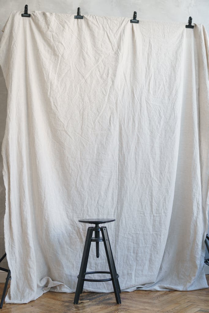 Simple studio setup featuring a metal stool and white fabric backdrop for photography.